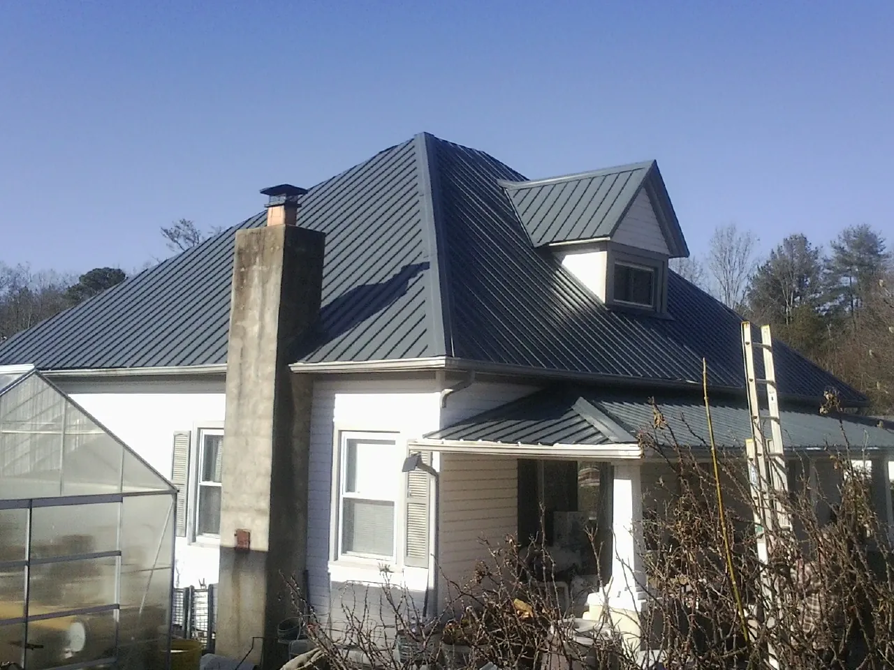 Dark blue standing seam metal roof on a white farmhouse with dormer — Slate & Tile Roof Repair by Roofing Brothers in Boothbay