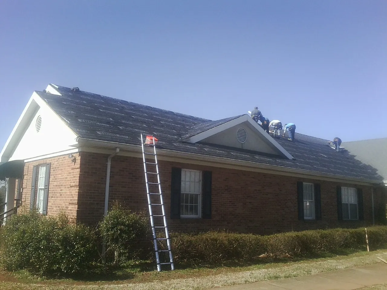 Crew tearing shingles off a brick ranch roof with a ladder set — Emergency Roof Repair work by our crew in Boothbay