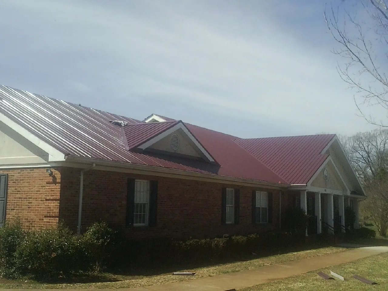 Red metal roof with gabled entries on a long brick building, from a Hail Damage Roof Repair job in Boothbay