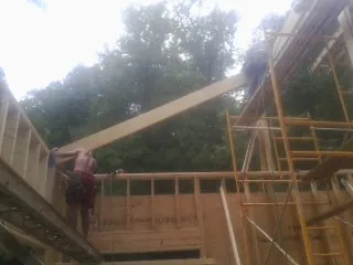 Carpenter raising a rafter beam on a new second story frame in Boothbay