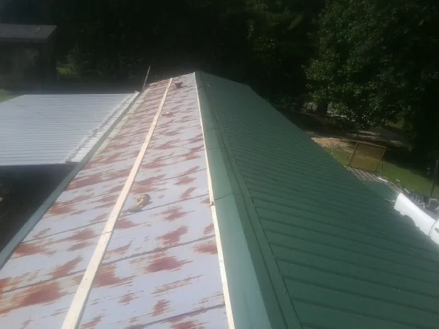 Old rusted panels beside newly installed green metal roofing — Wind Damage Roof Repair by Roofing Brothers in Boothbay