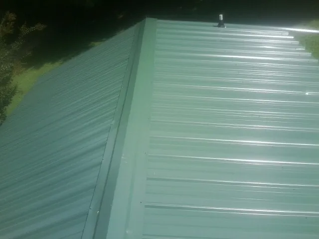 New green metal panels meeting at the ridge of a roof — Flat Roof Repair work by our crew in Boothbay