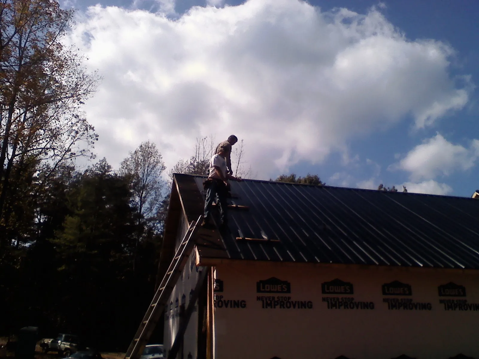 Roofer fastening dark metal panels high against a cloudy sky, from a Roof Inspection job in Boothbay